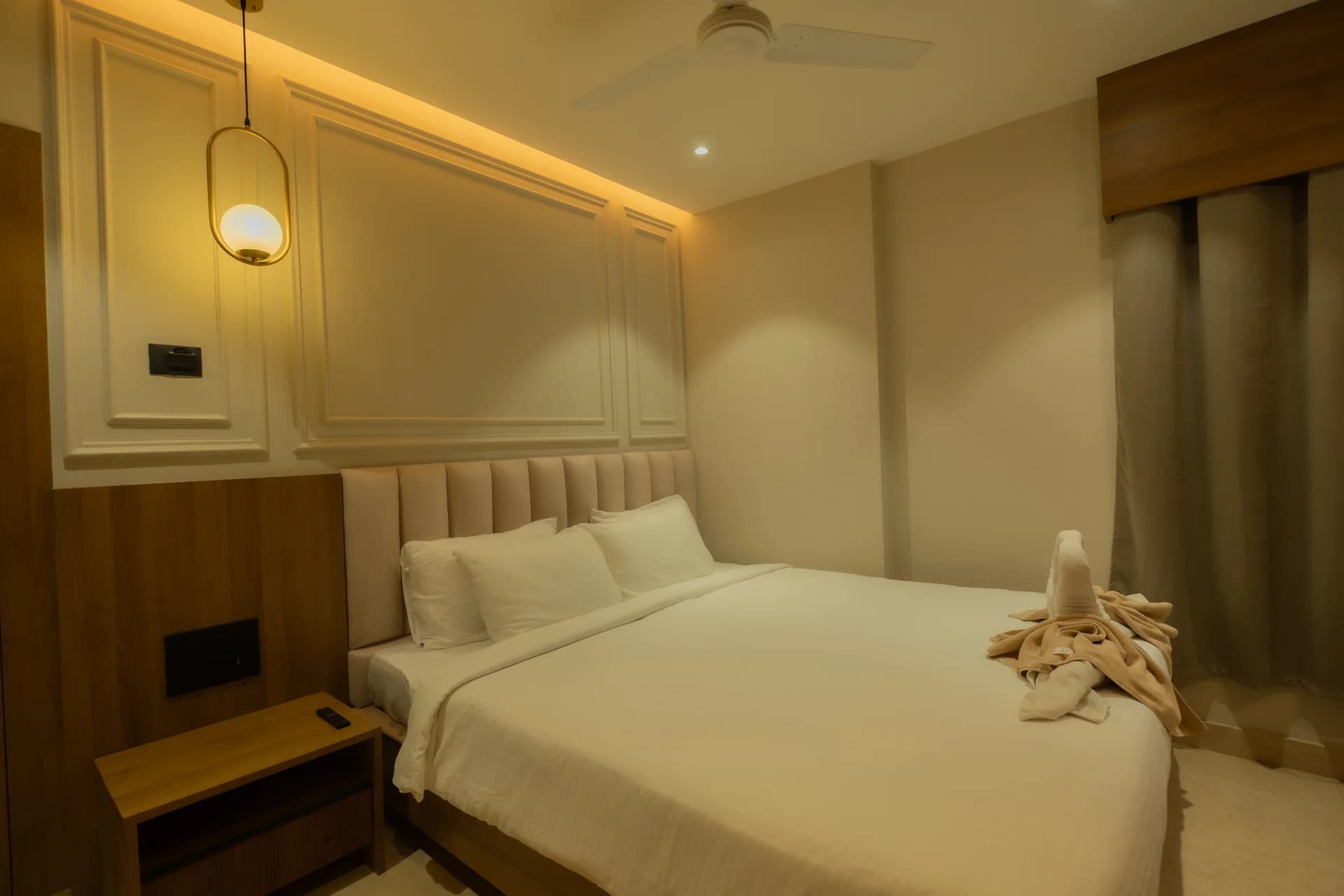 Ambika guest bedroom with a neatly made double bed, folded towels and warm pendant lighting