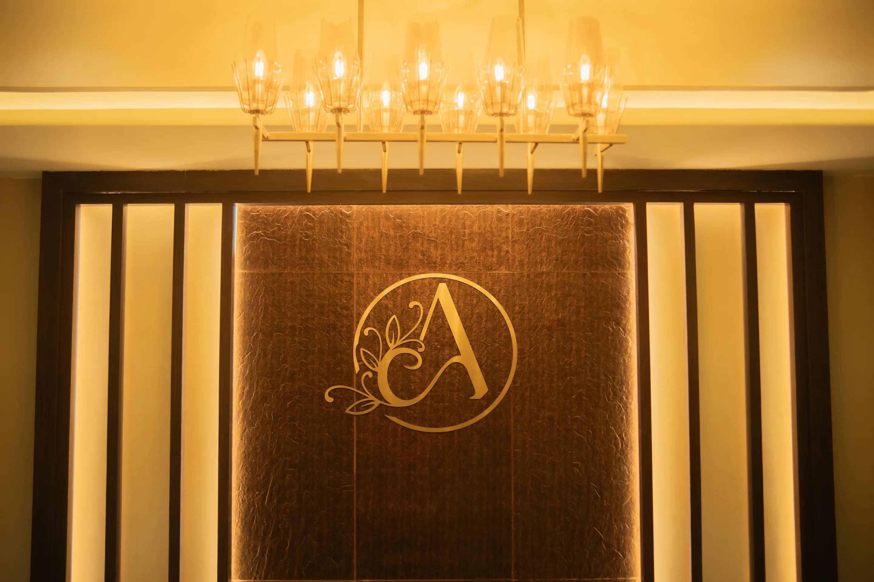 Gold Ambika monogram on the reception wall beneath a chandelier