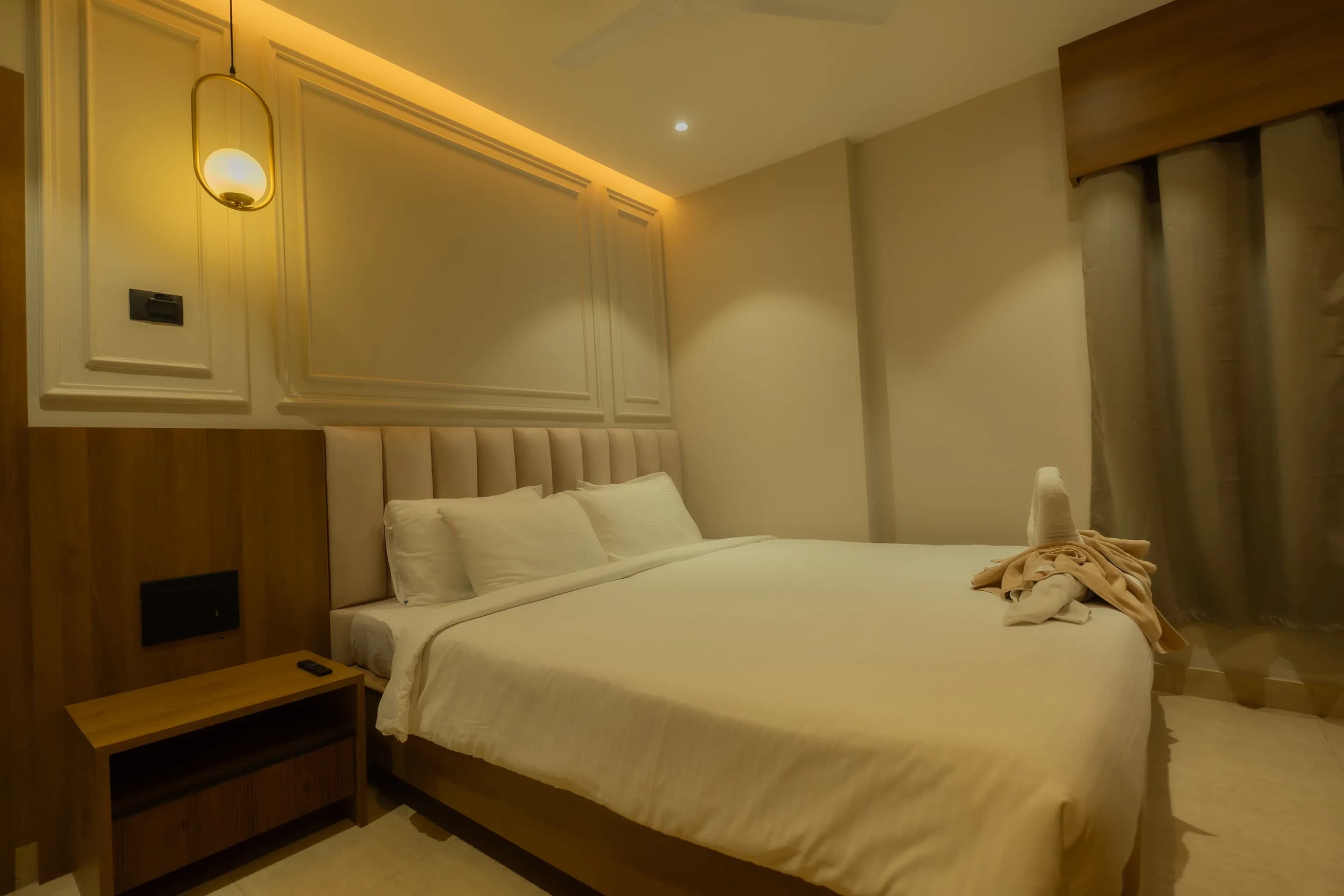 Guest room bed with warm headboard lighting and floor-length curtains