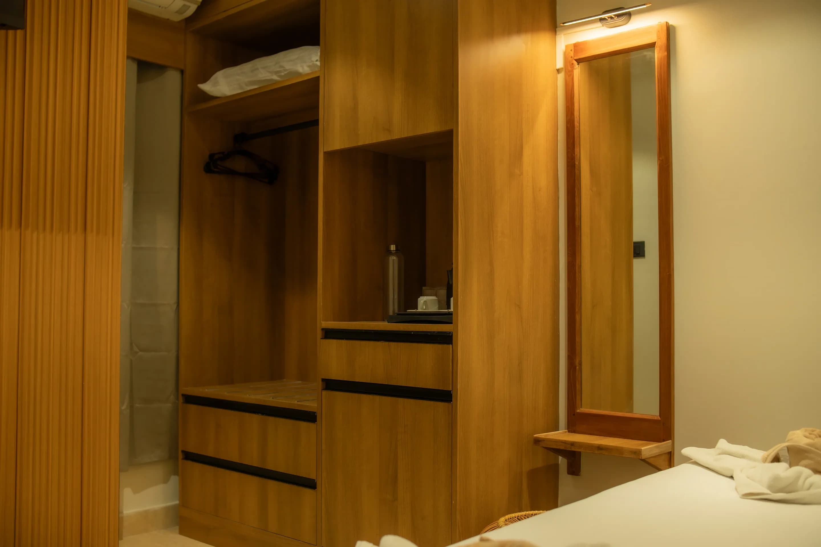 Guest room wardrobe and illuminated mirror above a woven stool