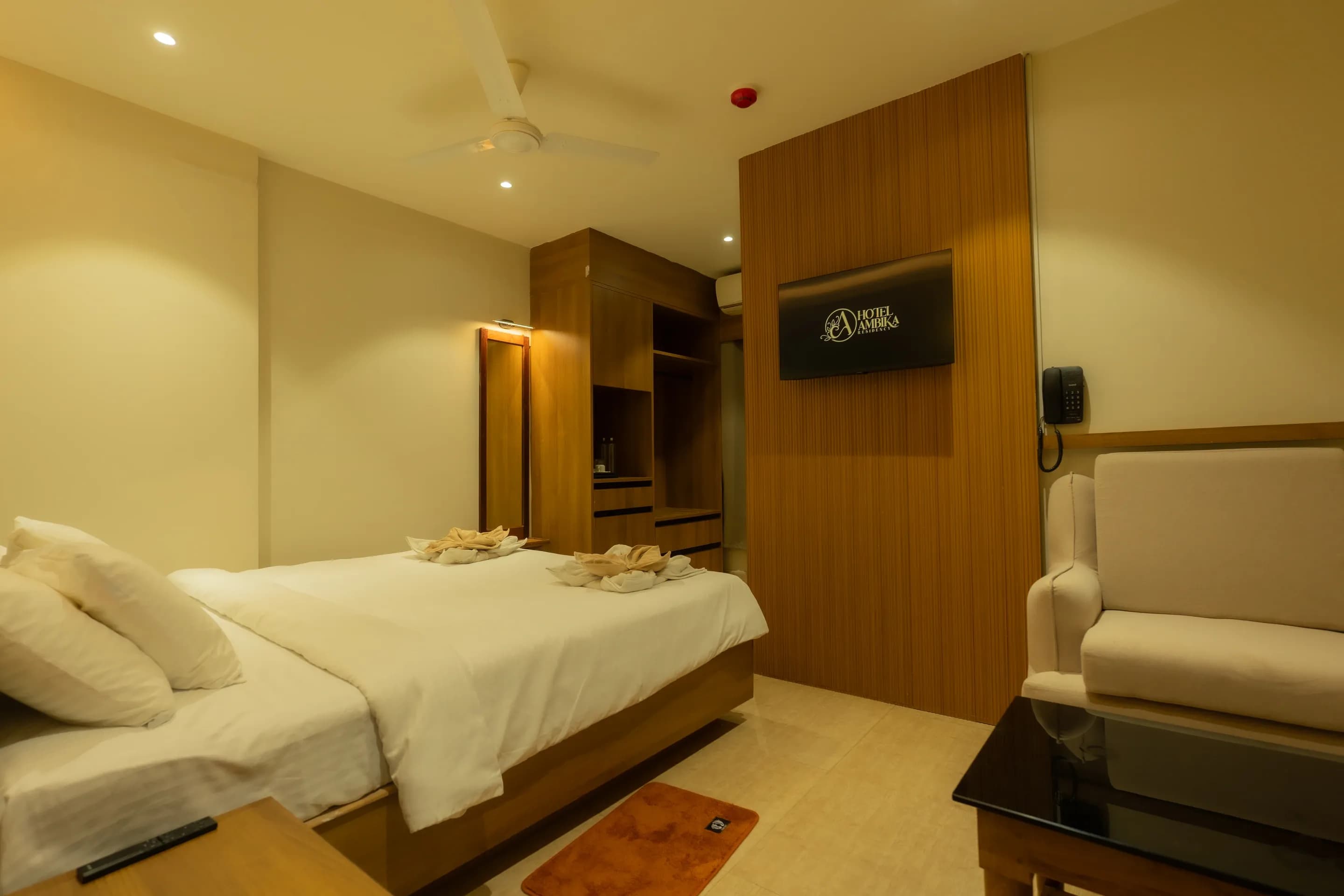 Wide guest room view showing the bed, television partition, wardrobe and armchair