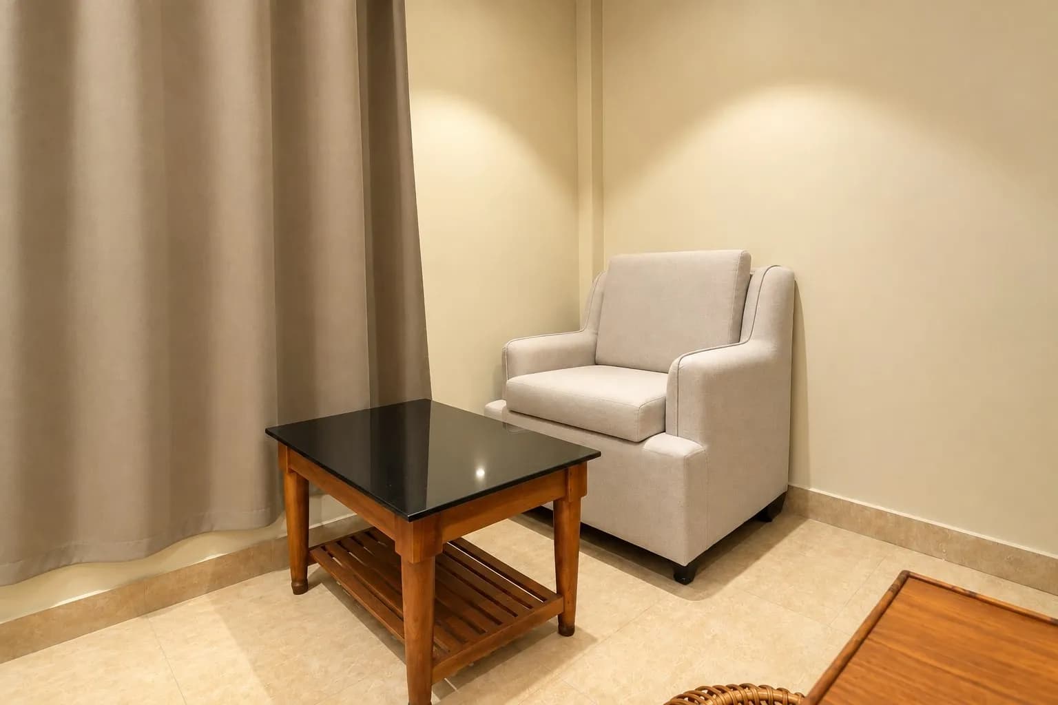 Upholstered armchair and glass-topped wooden table beside the room curtains