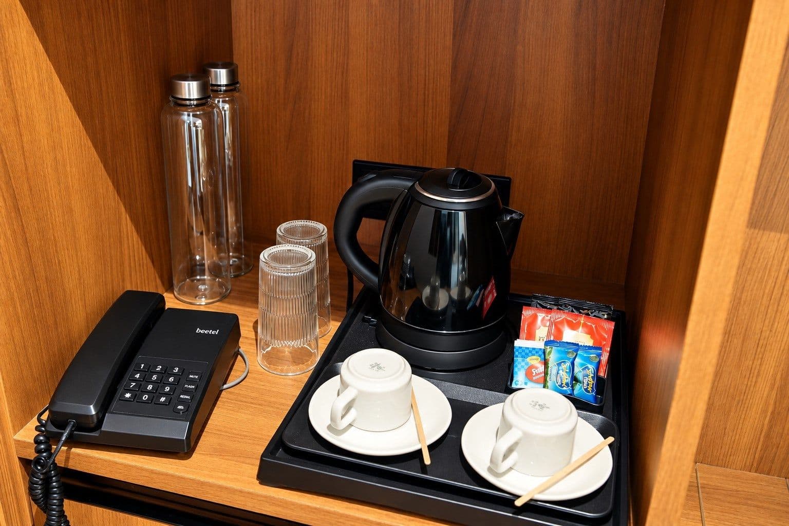 Kettle, bottled water, glassware and telephone in a room amenity niche