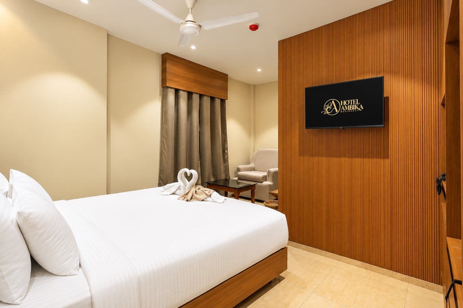 A guest room at Hotel Ambika Residency with a made bed, seating and curtains