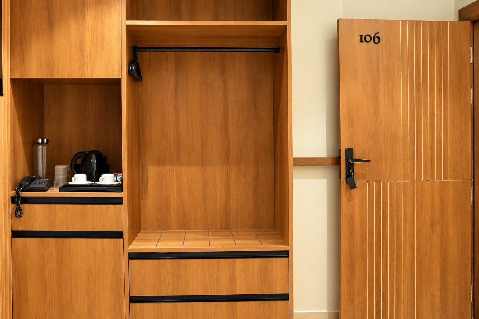 The room's open wardrobe niche holding the kettle, glassware, bottled water and telephone